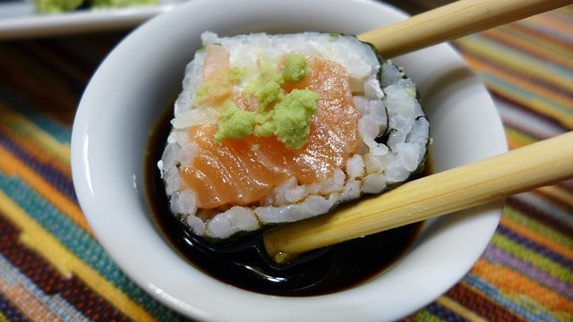 sushi dipped into soy sauce using wooden chopsticks